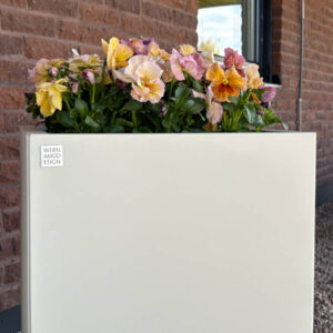 Beige planteringslåda med färgglada blommor från Wernamo Design mot tegelvägg